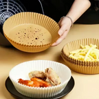 A person holds a beige fluted disposable baking-style bowl with food pieces inside, while another bowl of french fries and a white bowl sit on a tabletop nearby. A black appliance is partially visible in the background.