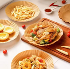 A styled food presentation featuring a whole roasted chicken with broccoli and peppers served on a brown paper plate, alongside french fries, mini tarts, and other dishes on matching Air Fryer Paper Tray and a wooden board.